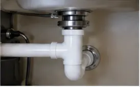 Plumber servicing a white drain trap beneath a bathroom vanity
